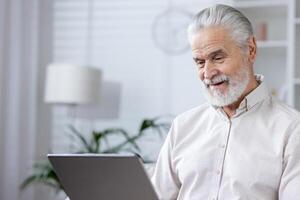 An elderly man working on a laptop in a well-lit room, reflecting an active, engaged lifestyle and modern work environment. photo