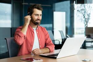 cliente Servicio representante con auriculares teléfono consulta cliente comprador, alegre hombre usos ordenador portátil para llamar, empresario en camisa a lugar de trabajo dentro oficina contento y sonriente. foto