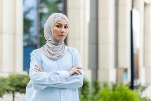 un profesional mujer en un hijab soportes con confianza con su brazos cruzado en un moderno ciudad ambiente, exudando seguridad en uno mismo y independencia. foto