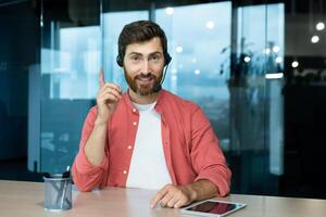 Webcam pov view, man in office with headset for call smiling and looking into camera, businessman seller online communicates with customers, works remotely laptop at online meeting colleagues photo