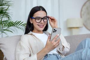 un contento joven mujer en cuarentena mentiras a hogar y comunica mediante un llamada desde el teléfono foto