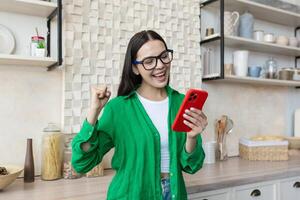 hermosa joven mujer en lentes y verde camisa leer bueno Noticias desde rojo teléfono foto