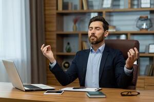 experimentado masculino profesional en un traje practicando atención plena meditación a su lugar de trabajo para relajación. foto