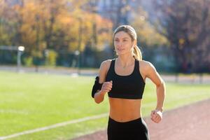 Female athlete is running in the stadium on a sunny day, woman in sportswear is active. photo