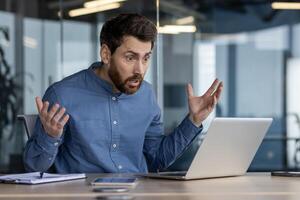 Shot of a startled male in an office setting, reacting with shock to something on his laptop screen. Captures the concept of unexpected news or error. photo