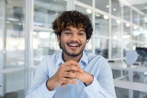 A young male professional with curly hair exudes confidence and happiness while seated in a bright, contemporary office environment. photo