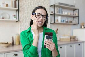 Young beautiful woman eating chocolate bar, having severe toothache at home. photo