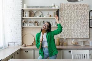 Young beautiful woman in glasses and green shirt in the kitchen having fun photo