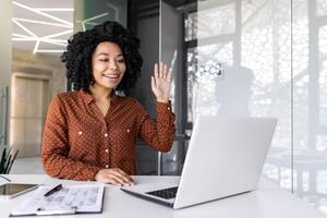 Successful curly black woman starting meeting on portable computer by desktop with writing board in office. Positive marketer connecting with remote colleague for new strategy consideration. photo