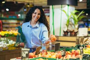 joven hermosa latín americano niña alumno, vegetariano elige y compra manzanas en el supermercado foto
