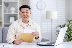 regocijado japonés empresario recepción postal letra y leyendo eso mientras trabajando por escritorio con ordenador personal. exitoso puesta en marcha propietario recepción banco notificación con préstamo aprobación para negocio desarrollando. foto