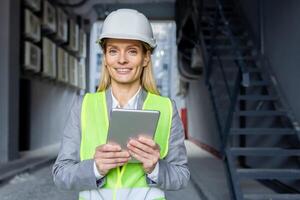 Professional caucasian woman in helmet and neon yellow vest standing at construction with digital tablet in hands. Experienced female architect checking house building process and entering data. photo