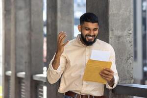 Happy man with beard receiving good news in mail envelope outdoors photo