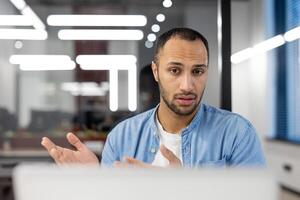 A professional businessman in a modern office appears confused while staring at his computer screen, expressing problem-solving and concentration. photo