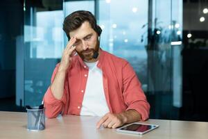 cámara web vista, remoto llamar, triste hombre con auriculares sentado tarde a lugar de trabajo, sobrecargado de trabajo y sobrecargado de trabajo cliente apoyo obrero. foto