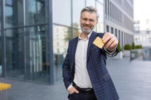 A smiling businessman in a suit holds a card in his hands, stands on the street in front of the office, looks at the camera. photo