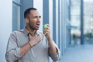 Sick man outside office building has severe sore throat, businessman outside office building uses aerosol medicine for throat photo