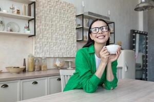 Young woman, mother drinks coffee, tea alone in the kitchen at home. He holds a cup in his hands photo