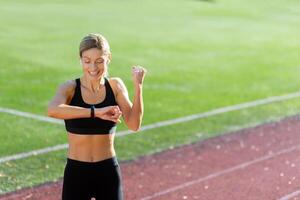 Satisfied with the result of training and running, the athlete looks at the smart watch, the blonde holds her hand up and celebrates the victory. photo