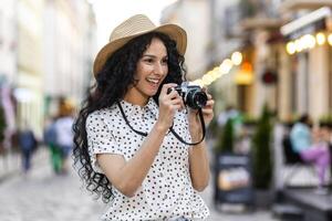 joven hermosa Hispano mujer con Rizado pelo caminando en el noche ciudad con un cámara, hembra turista en un viaje explorador histórico puntos de referencia en el ciudad. foto