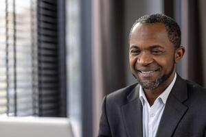 Confident African American businessman in a formal suit standing in a modern corporate office environment. photo