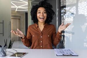 entusiasta joven mujer en un polca punto blusa negociaciones y gestos animadamente durante un conferencia a su moderno espacio de trabajo foto