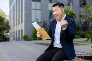 Joyous man in business attire receiving great news from a letter, showing an emotional victory gesture. photo