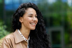 retrato de un feliz, atractivo mujer con hermosa Rizado pelo sonriente fuera de con verdor en el antecedentes. foto