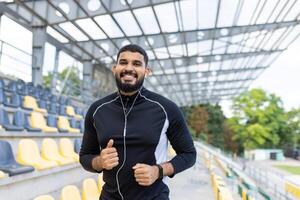 un ajuste masculino corredor con auriculares trota en un estadio pista, exhibiendo un sano estilo de vida y determinación. foto