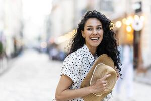retrato de un joven hermosa mujer en un sombrero, un turista es caminando en el noche ciudad, alegremente mirando a el lado con Rizado cabello. foto