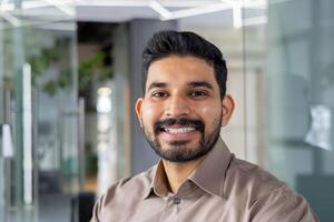 Portrait of a cheerful young man wearing a light brown shirt, smiling confidently in a contemporary office setting. Perfect image for business and lifestyle themes. photo