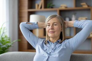 Mature woman enjoying a peaceful moment at home, sitting back with eyes closed. Capturing a sense of relaxation and contentment in a cozy living room setting. photo