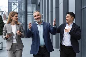 un diverso equipo de eso especialistas, mayor y experimentado ingenieros gerentes equipo líderes, un grupo de Tres trabajadores felizmente vagante fuera de un oficina edificio, colegas en negocio trajes. foto