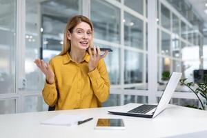 Portrait of a young business woman sitting in the office at the desk and talking on the phone through the loudspeaker with clients and partners. photo