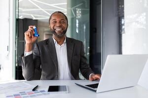 retrato de satisfecho tratado hombre dentro oficina, empresario sonriente y mirando a cámara, participación inhalador para respiración alivio y asma a lugar de trabajo. foto