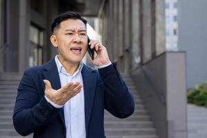 un agitado profesional hombre en un formal traje comunica terminado un célula teléfono con un descontento expresión. foto