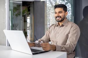 Happy young businessman working on laptop at desk in contemporary office setting, showing job satisfaction and professionalism. photo