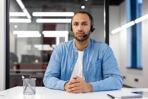 Portrait of a serious Muslim man sitting at a desk in the office, wearing a headset, confidently looking at the camera. photo