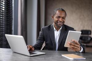 Smiling male in white shirt and black jacket using two electronic gadgets for optimisation of working process. Contemporary entrepreneur connecting to crm system of company for online interacting. photo