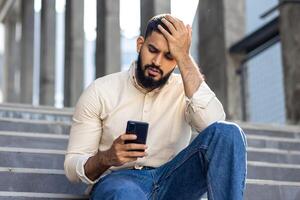 hombre en casual atuendo sentado en escalera al aire libre con teléfono inteligente foto