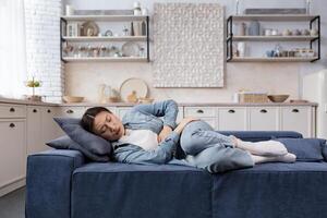 Sick and sad woman lying on the sofa at home in the living room Asian woman has severe stomach pain photo