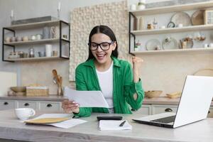 Happy woman in glasses and green shirt at home doing paper work got good result photo