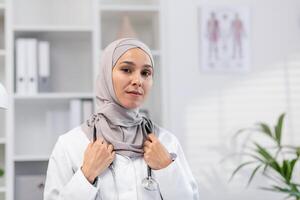 un retrato de un elástico y confidente musulmán hembra médico vistiendo hijab en un bien equipado médico oficina, exudando profesionalismo y cuidado. foto