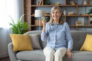 Mature woman smiles as she uses a medicine spray for sore throat at home, showcasing self-care and healthcare. photo
