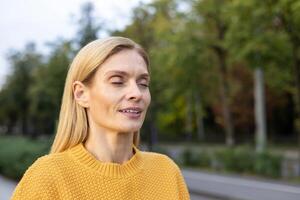 de edad mediana mujer disfruta un pacífico momento con su ojos cerrado, rodeado por lozano verdor en un tranquilo parque. sentimientos de serenidad y contentamiento. foto