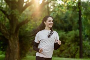 Young beautiful woman running in the evening in the park, hispanic woman with curly hair smiling contentedly, active lifestyle photo
