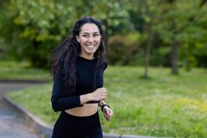 An enthusiastic female runner with a bright smile and long curls jogs in nature, exuding fitness and well-being. photo
