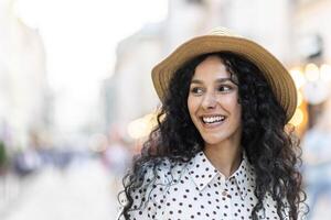 Portrait of a young beautiful woman in a hat, a tourist is walking in the evening city, joyfully looking to the side with curly hair. photo