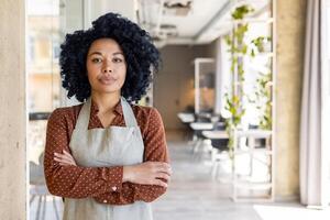 Portrait of a serious and self-confident African-American businesswoman, owner of a restaurant, bar, standing with her arms crossed and looking at the camera. photo