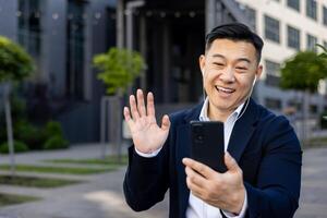 Happy professional man engaging in a call, waving hello to colleagues with earphones and a smile outside. photo